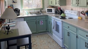 Een keuken met groene kastjes, een witte kookplaat, een magnetron en een spoelbak.