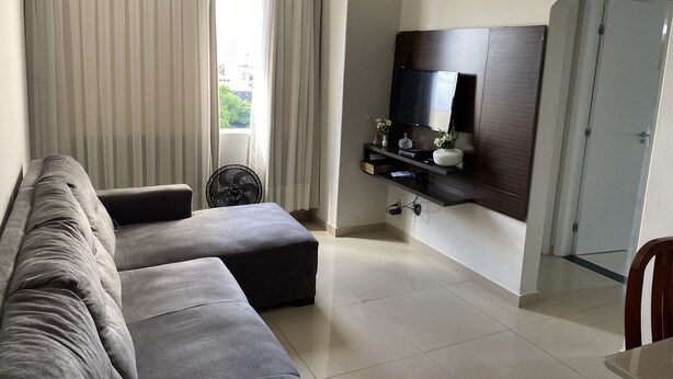 A modern living room with a grey sofa, a small table, a wall-mounted TV, and a door.