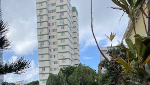 A playground with a slide and climbing structures, surrounded by a grassy area with trees and a tall building in the background.