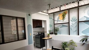 Une cuisine de taille réduite, équipée d’une cuisinière, de placards et d’une fenêtre où est suspendue une plante.