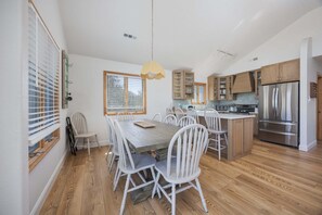 Una cocina moderna con suelo de madera, sillas blancas, una isla central y electrodomésticos de acero inoxidable.