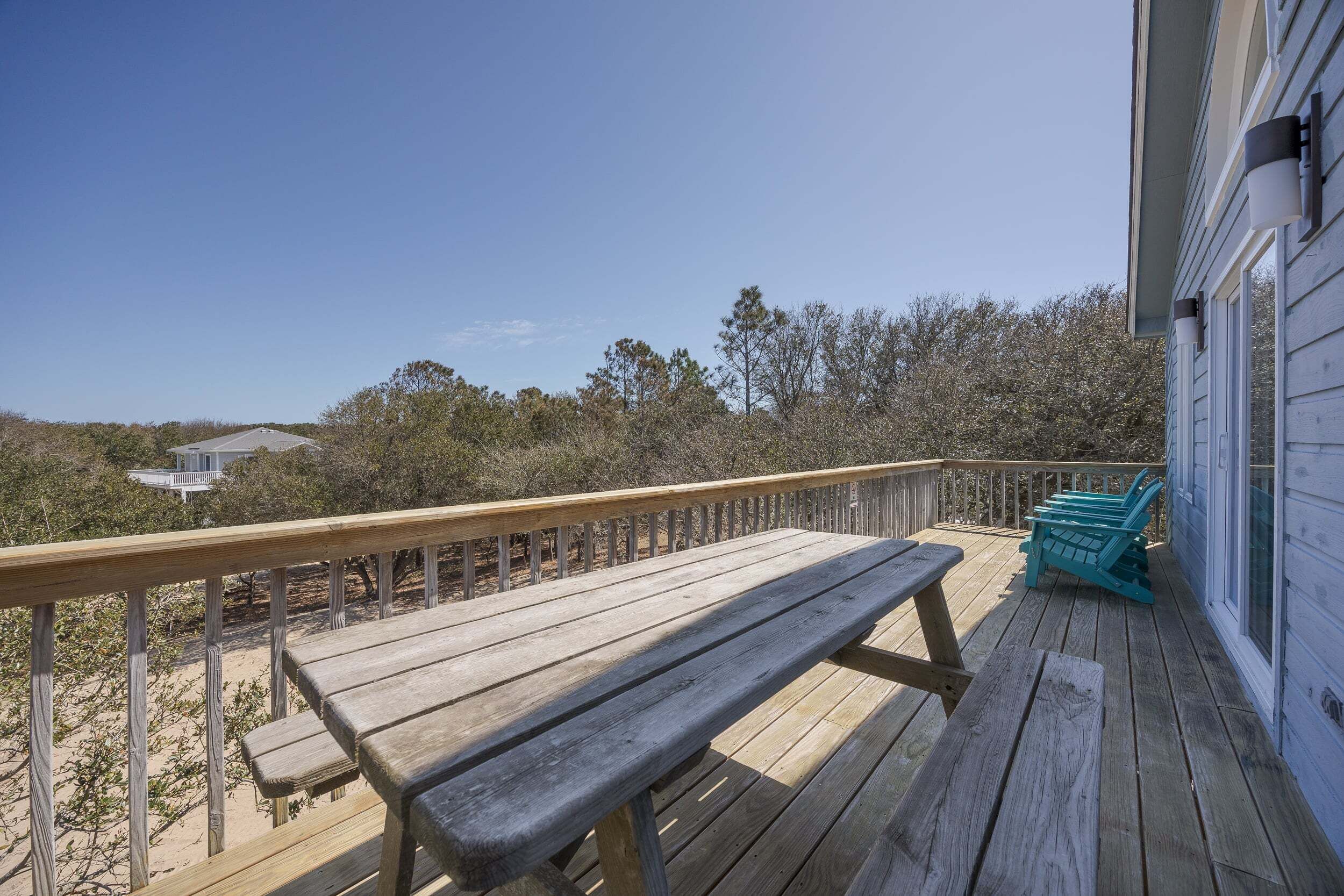 Une terrasse en bois avec un banc et des chaises, donnant sur une plage et des arbres.