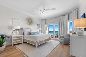 Une chambre à coucher moderne, dotée d’un lit, de tables de chevet, d’un ventilateur de plafond et offrant une vue sur l’océan.