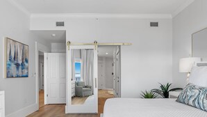 A modern bedroom with a large bed, a sliding door closet, a painting, and a view of another room. - "Beach DNA" at The Legacy 203 in Seagrove Beach | My Beach Getaways (Santa Rosa Beach)