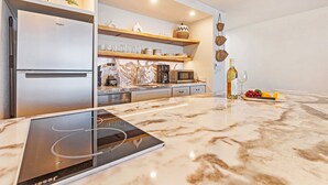Una cocina moderna con refrigerador, microondas y cafetera incorporados. Hay estantes de madera sobre la encimera con diversos utensilios de cocina.