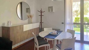 A dining area with a round table, white chairs, a wooden cabinet, a coat rack, and a hanging light fixture. - Holiday apartment 200 m to the beach (Sirmione)