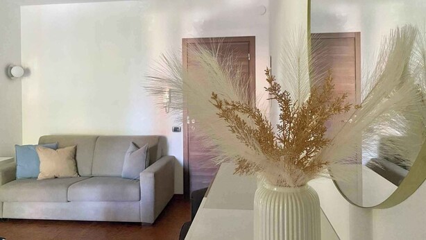 A living room with a sofa, a vase with dried plants, and a mirror reflecting the room. - Holiday apartment 200 m to the beach (Sirmione)