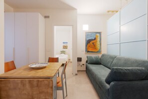 Een moderne woonkamer met een houten eettafel, een groene bank en een schilderij aan de muur.