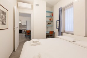 Een hotelkamer met een bed, een bureau, een stoel, een kleine kitchenette en een raam met gordijnen.