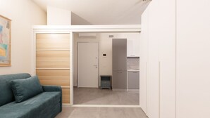 Un espacio habitable compacto con sofá, kitchenette y una puerta que conduce a otra habitación.