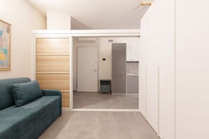 Un espacio habitable compacto con sofá, kitchenette y una puerta que conduce a otra habitación.