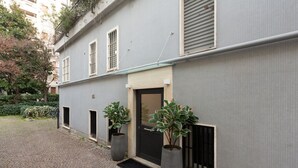 Un edificio de fachada gris, una puerta negra y dos macetas con plantas.