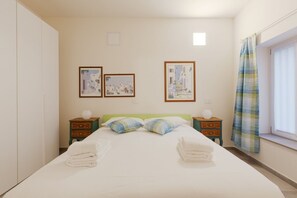 A hotel room with a bed, two nightstands, a window with a curtain, and two framed pictures on the wall.