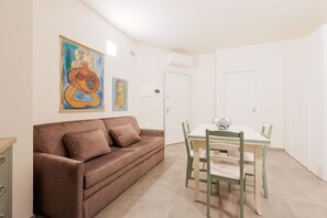 A room with a brown sofa, a dining table with chairs, and two doors.