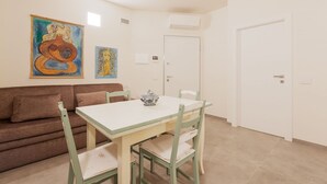 Una habitación con una mesa blanca, sillas verdes, un sofá marrón y dos cuadros en la pared.