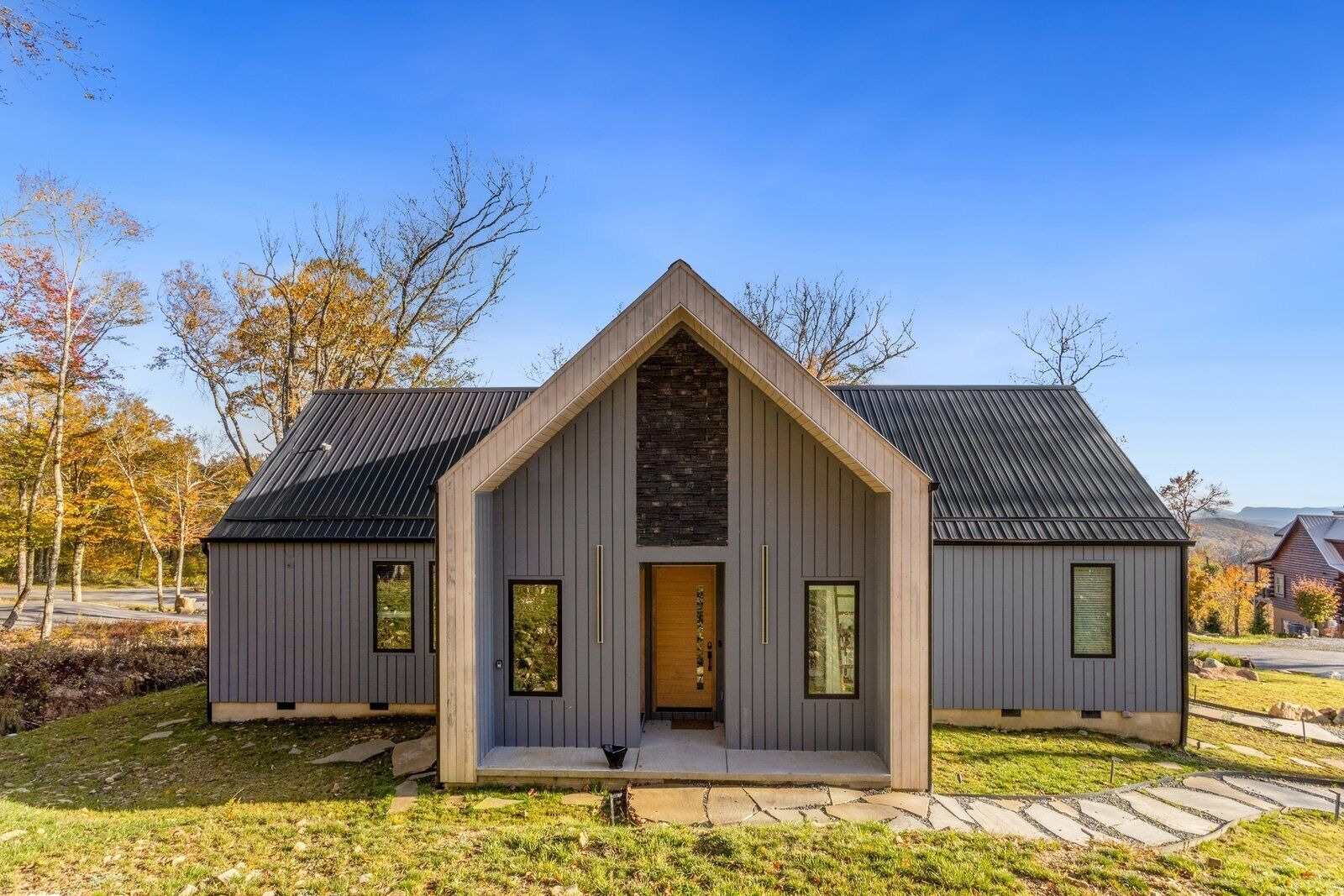 Une maison moderne avec un toit à pignon, un mur d’accent en pierre et un porche à l’avant.