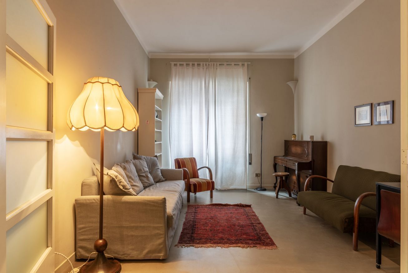 A living room with a sofa, armchairs, a coffee table, a lamp, a piano, and a red rug.