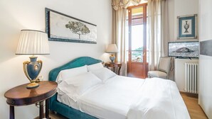 Habitación de hotel con una cama, dos mesitas de noche, una lámpara, un cuadro enmarcado, un televisor y una ventana con cortinas.