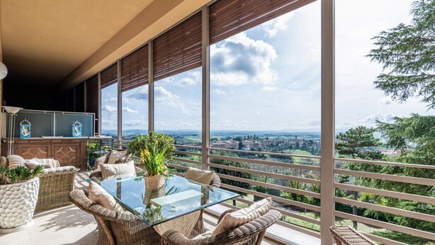Un balcón con mobiliario de mimbre, una mesa de vidrio y vistas a un paisaje lejano.