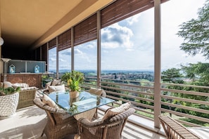 A balcony with wicker furniture, a glass table, and a view of a distant landscape.