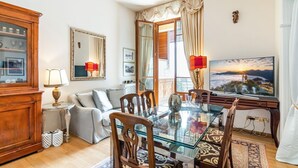 Una sala de estar con una mesa de comedor de vidrio, sillas de madera, un sofá, un televisor y un mueble de madera.