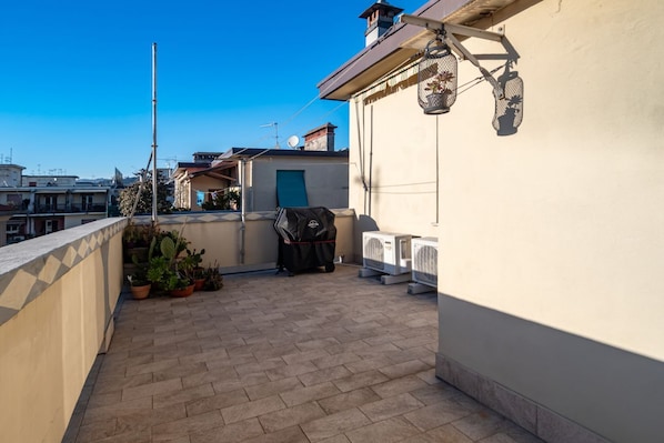 A rooftop terrace with potted plants, a grill, and a washing machine.