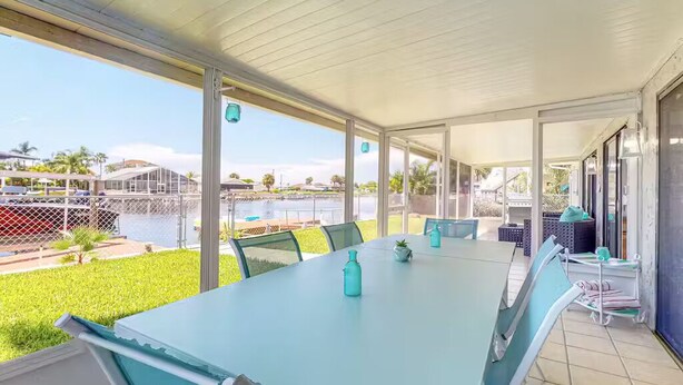 A covered outdoor dining area with a long table, chairs, and a view of a body of water and greenery. - Waterfront home with direct gulf access   (Hernando Beach)