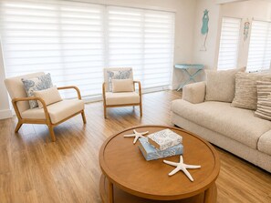 Una sala de estar con un sofá beige, dos sillones, una mesa de centro de madera y una mesita con un objeto decorativo.