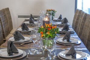 A dining table set for a meal with plates, cutlery, and glasses, surrounded by wicker chairs.
