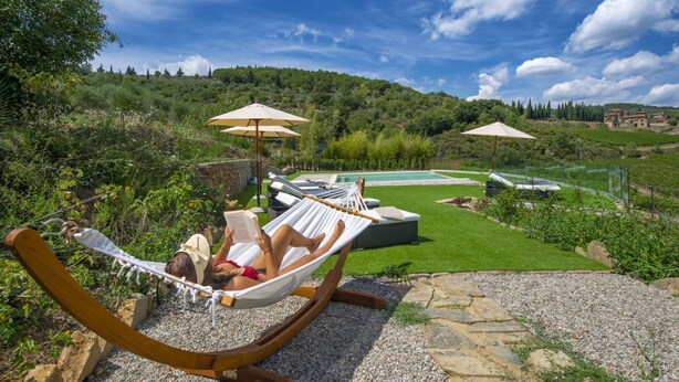 Une personne se détend dans un hamac, un livre à la main, avec vue sur une piscine et une végétation luxuriante.