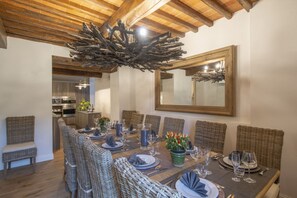 Un comedor con una mesa larga dispuesta para seis personas, rodeada de sillas de mimbre, techo de madera y un espejo grande en la pared.