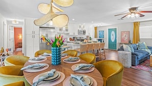 A modern kitchen with white cabinets, a dining area with yellow chairs, and a living room with a blue sofa.