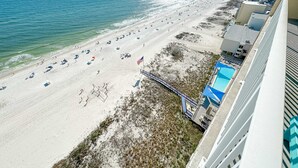A beach view from a hotel balcony with a pool and beach umbrellas. - BEACHFRONT, ZERO ENTRY POOL, PRIVATE BALCONY! (Gulf Shores)