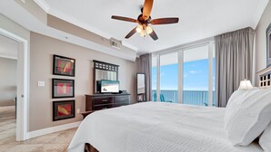 A spacious bedroom with a large bed, a ceiling fan, a flat-screen TV, and a view of the ocean. - BEACHFRONT, ZERO ENTRY POOL, PRIVATE BALCONY! (Gulf Shores)