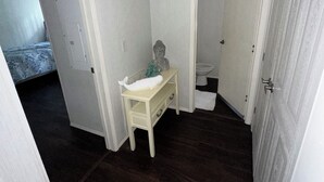 Een kleine, smalle kamer met een witte wastafel, een beeld en een donker houten vloer.