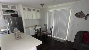 Een compacte keuken met witte kastjes, een koelkast, en een eethoek met een glazen tafel en stoelen.