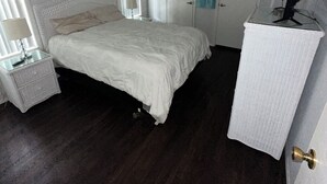 Een slaapkamer met een bed, nachtkastje, bureau, plafondventilator, raam met jaloezieën en een deur.
