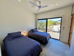 Une chambre avec deux lits, un ventilateur de plafond, une fenêtre donnant sur l’extérieur et une porte.