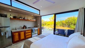 Une chambre d’hôtel moderne dotée d’un grand lit, d’une kitchenette et d’un balcon avec vue sur la piscine.
