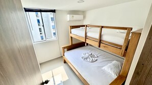 Ett litet, rent rum med en våningssäng, ett fönster med luftkonditioneringsaggregat och en väggmonterad luftkonditioneringsanläggning.