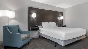 A modern hotel room with a large bed, a blue armchair, bedside tables, and wall-mounted lamps.