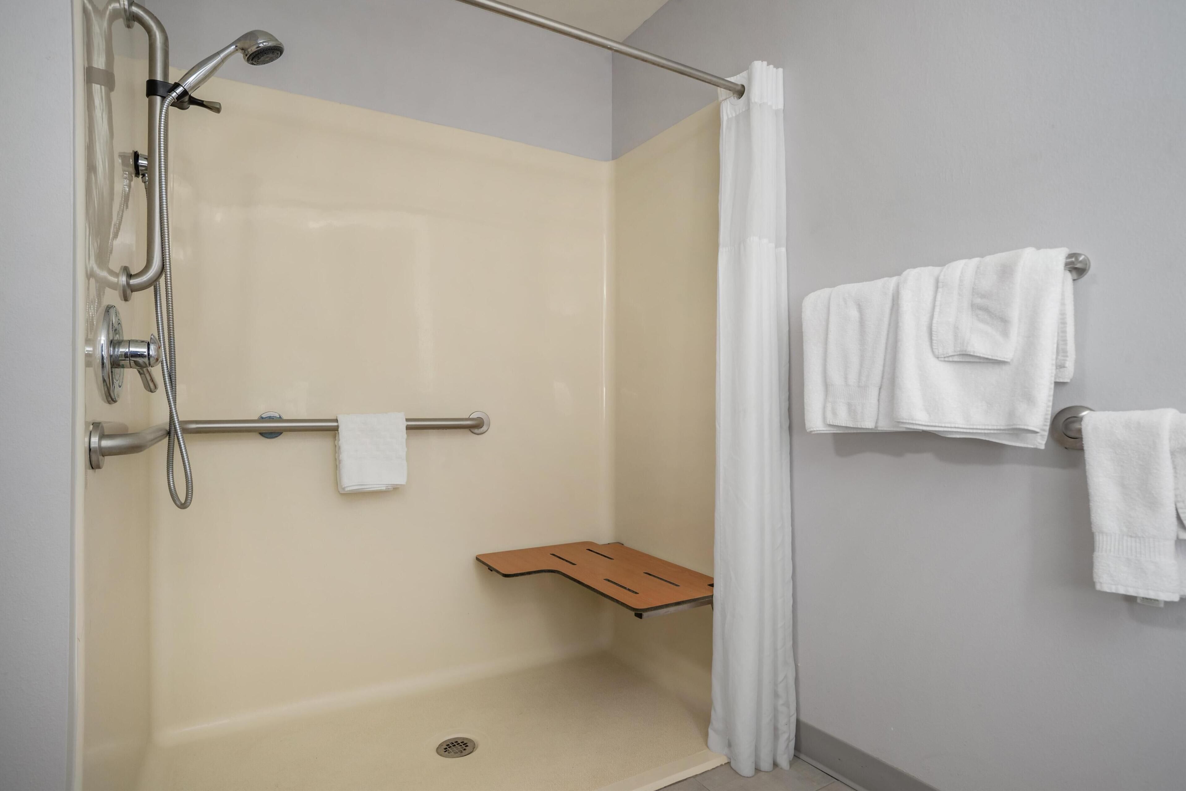 A shower with a handheld showerhead, a handheld shower attachment, a towel rack with two towels, and a wooden shelf.