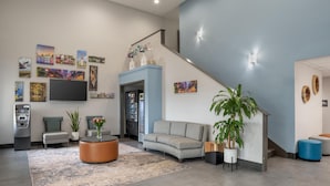 A modern lobby with a grey sofa, a round coffee table, a staircase, and a flat-screen TV mounted on the wall.