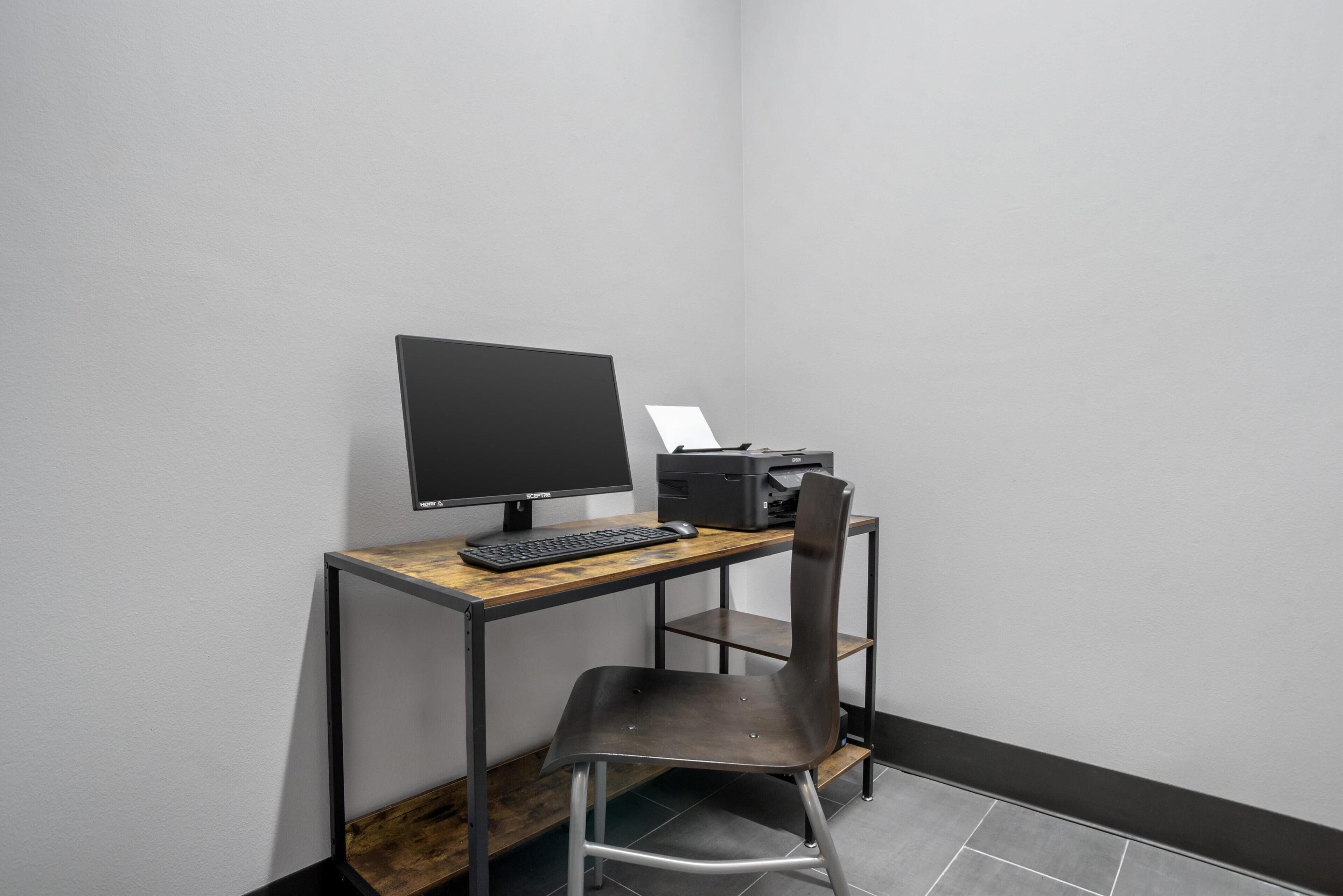 A small, modern office space with a desk, computer monitor, keyboard, and printer.