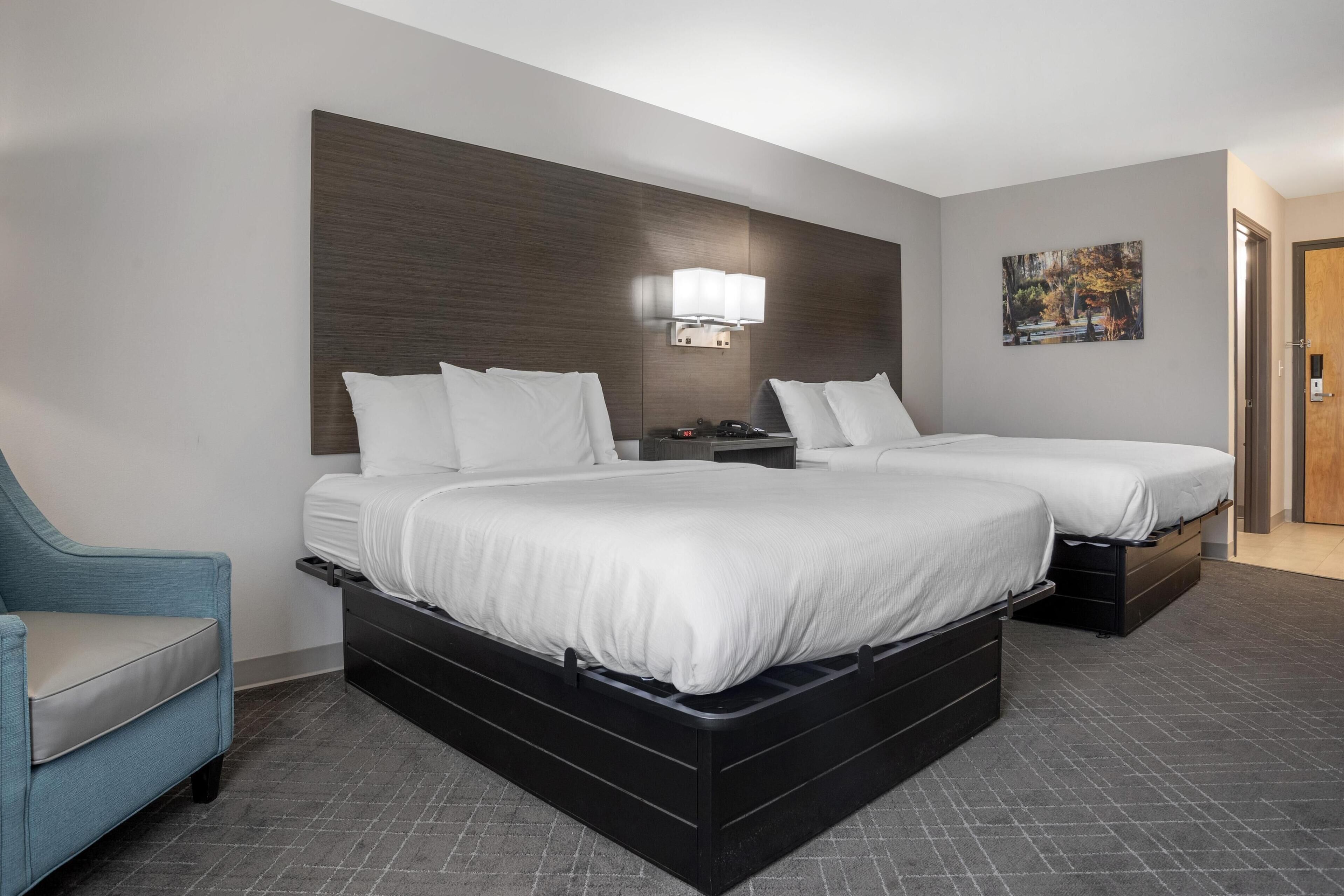 Een hotelkamer met een groot bed, een nachtkastje, een stoel en een schilderij aan de muur.
