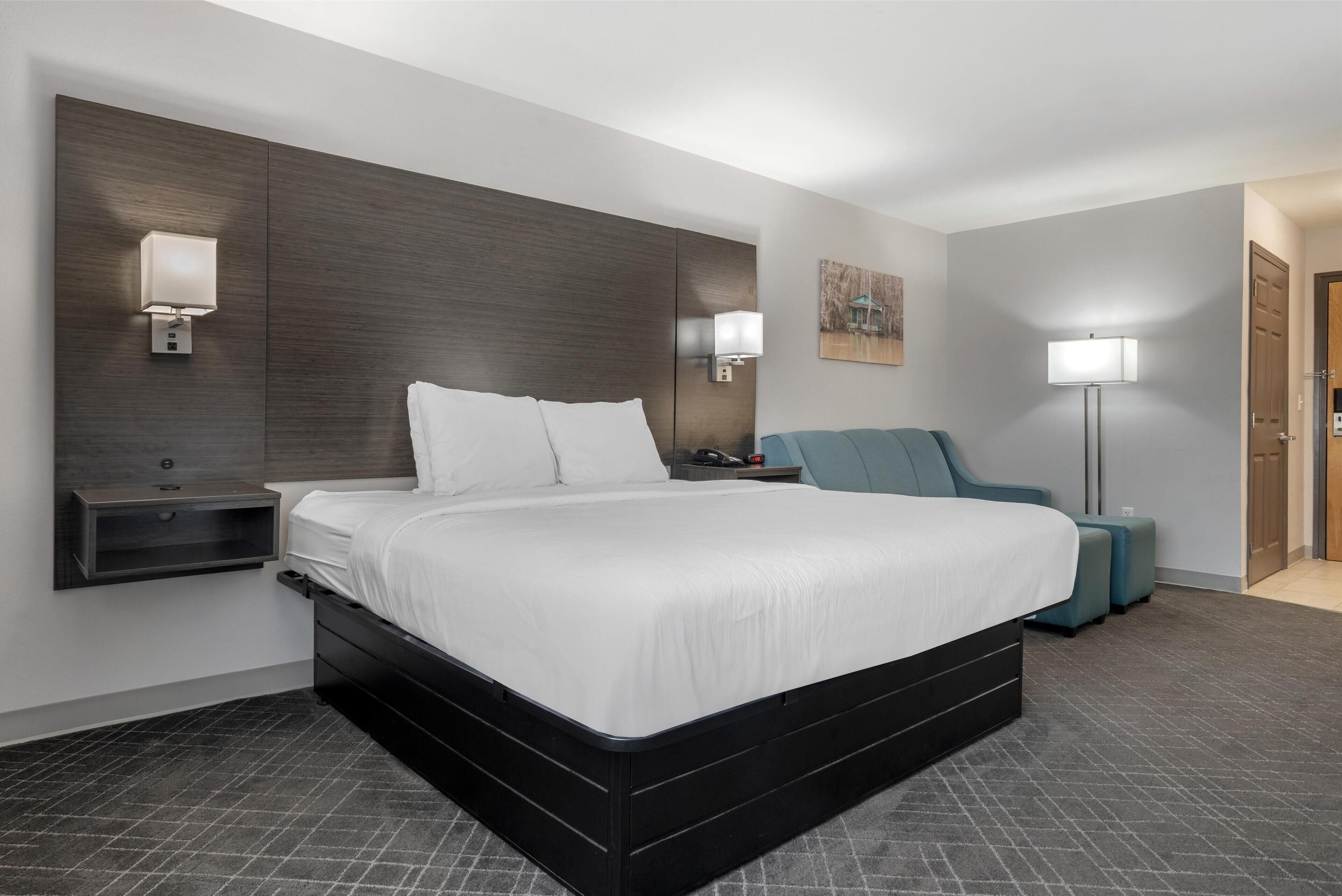 A modern hotel room with a large bed, bedside tables, a chair, and a floor lamp.