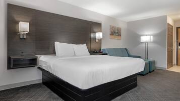 A modern hotel room with a large bed, bedside tables, a chair, and a floor lamp.