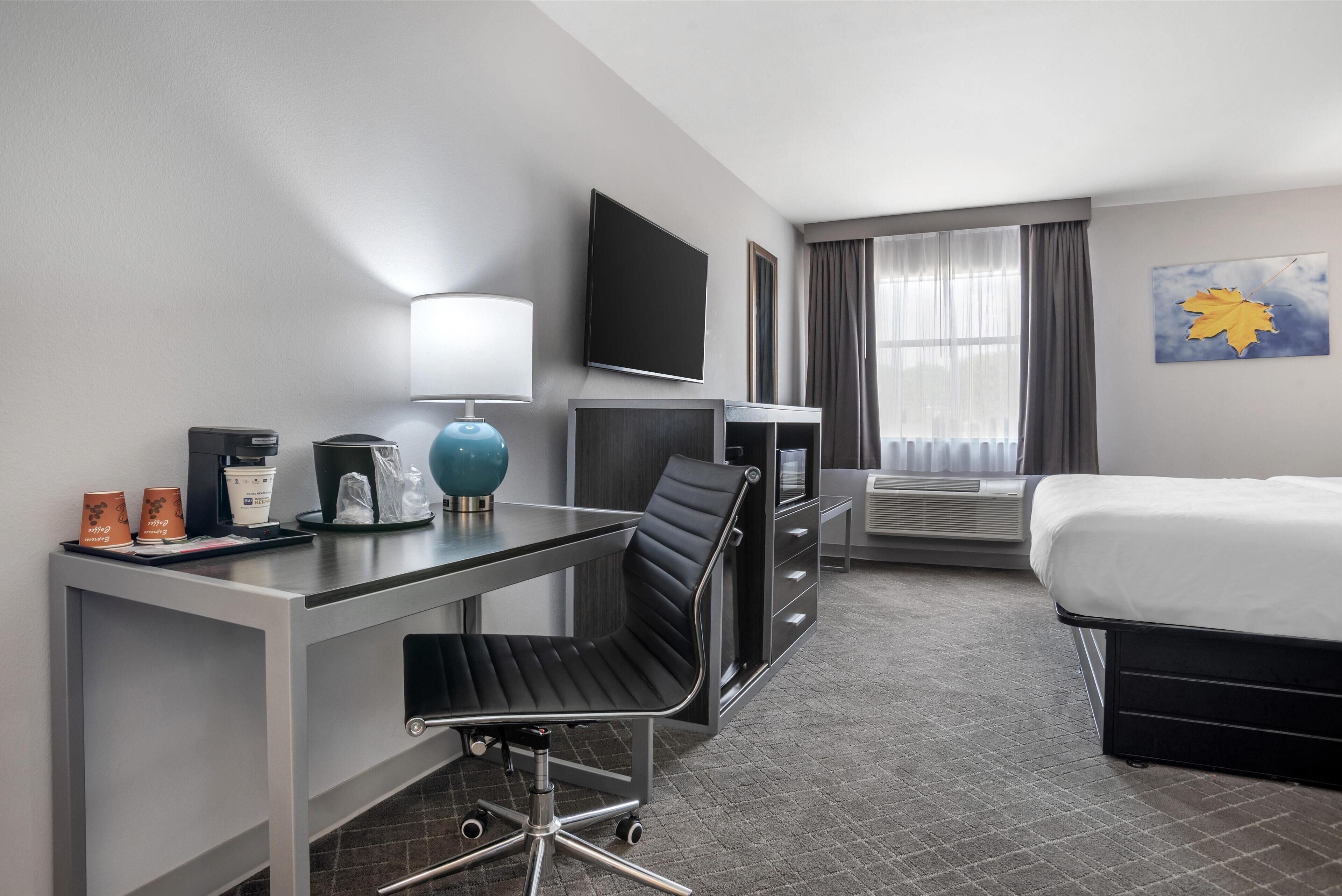 A hotel room with a desk, chair, bed, TV, and a window with curtains.
