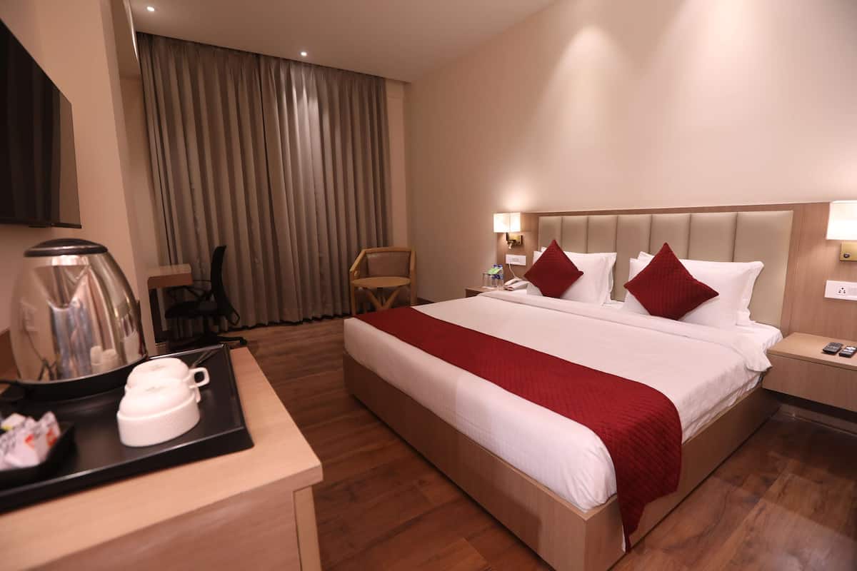 Habitación de hotel con cama, mesita de noche, silla, escritorio con cafetera y ventana con cortinas.