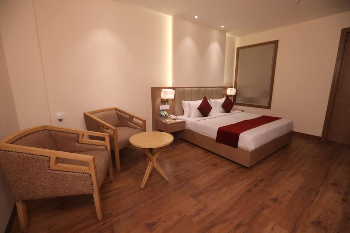 Una habitación de hotel con una cama, dos sillas, una mesita pequeña y una mesita de noche.